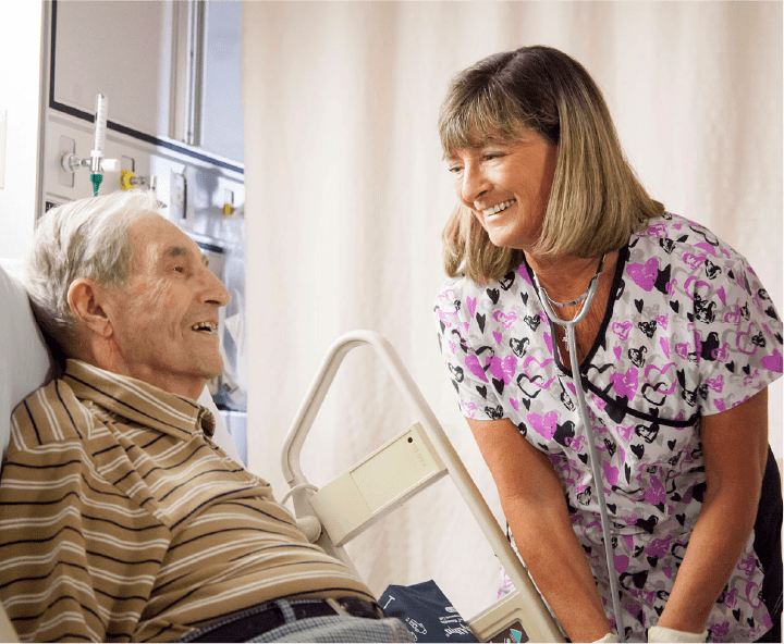 Nurse helping bedridden elderly man laying in hospital bed